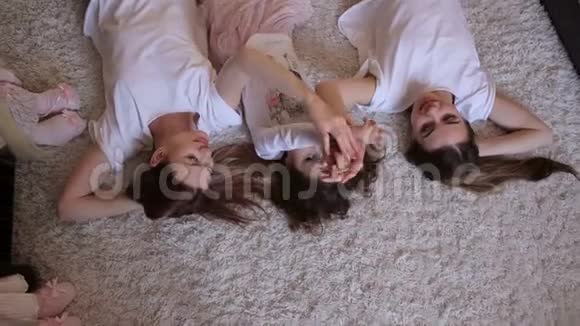 三个不同年龄的姐妹躺在地板上铺着蓬松的地毯哈哈大笑视频的预览图