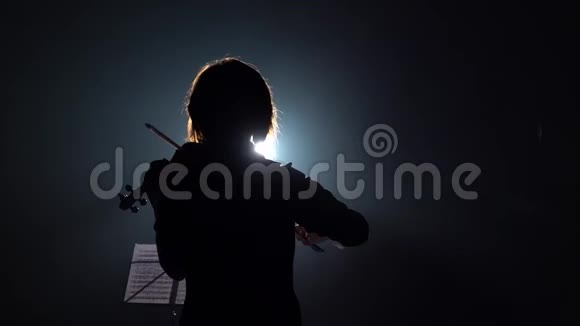 音乐家一边拉小提琴一边背着他站着黑烟背景背面视频的预览图