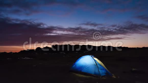 在山上夕阳的背景下照亮了蓝色的帐篷视频的预览图