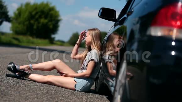 一个金发女孩坐在她那辆破车旁边的马路上视频的预览图
