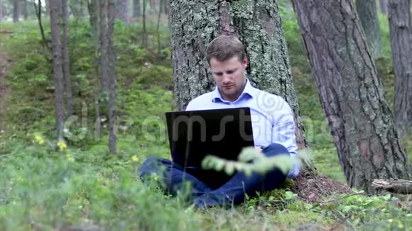 在树林里树下操作笔记本电脑的自由职业者视频的预览图