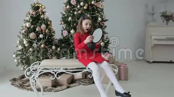 穿红衣服的女孩坐在家里靠近圣诞树的长凳上玩镜子圣诞节视频的预览图