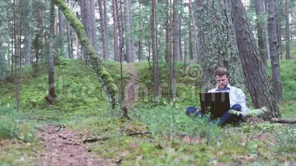 一个在森林里树下用笔记本电脑工作的人视频的预览图