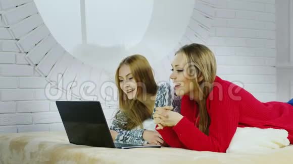 两个穿着家装的可爱女友躺在床上和朋友在skype上聊天视频的预览图