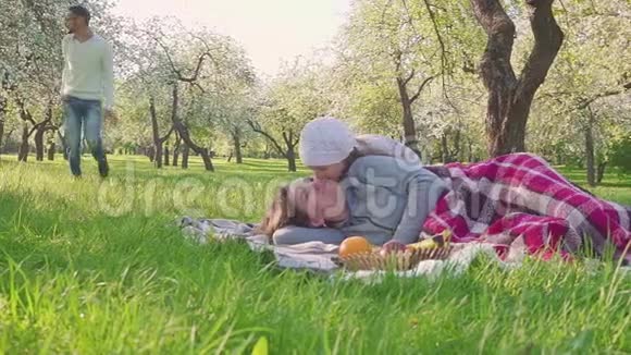 幸福的家庭花时间在盛开的苹果树附近野餐母亲躺在草地上孩子和丈夫跑视频的预览图