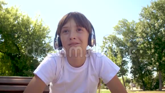 一个漂亮的女孩坐在公园的长凳上通过麦克风和耳机交谈视频的预览图