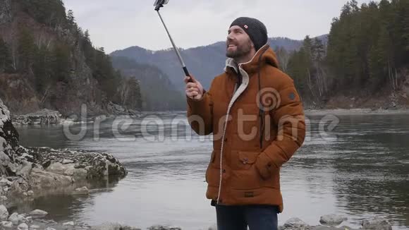 大胡子的游客正在一条山河的河岸上用手机播放视频慢动作视频的预览图