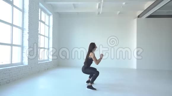 侧面观看瘦削迷人的女运动员在白色工作室做跳跃蹲视频的预览图