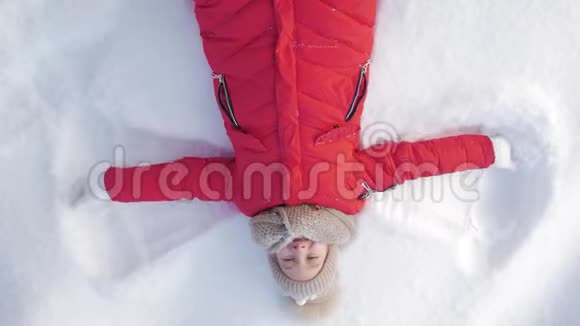 快乐的女孩躺在雪地上展示天使一个穿外套的漂亮女孩躺在雪地上张开双臂视频的预览图