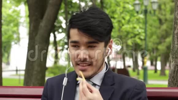 亚洲男商人坐在公园里吃炸薯条视频的预览图