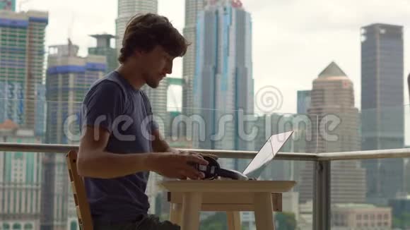 年轻的自由职业者在阳台上的笔记本电脑上工作背景是一个充满摩天大楼的市中心远程视频的预览图