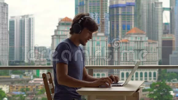 年轻的自由职业者在阳台上的笔记本电脑上工作背景是一个充满摩天大楼的市中心远程视频的预览图