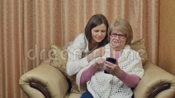 开朗的母女享受视频通话看着智能手机屏幕微笑着坐在家里的椅子上视频的预览图