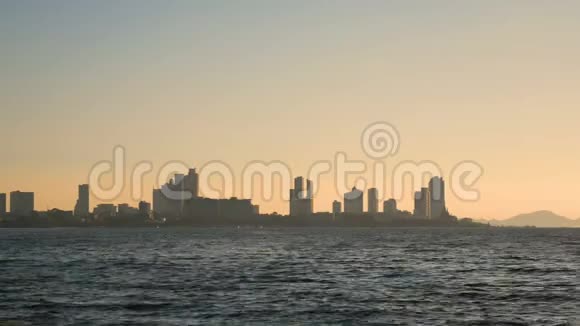 4K镜头的城市海岸景观与许多大建筑和蓝色的海洋与海波前景与橙色的光后城市视频的预览图
