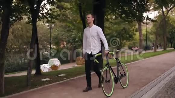 穿着白色衬衫的白种人满脸笑容的年轻人骑着自行车在城里的大街上散步把他的视频的预览图