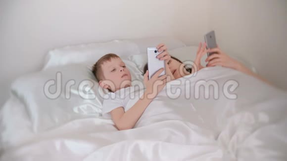 妈妈和儿子醒来在他们的手机上浏览互联网前视图视频的预览图
