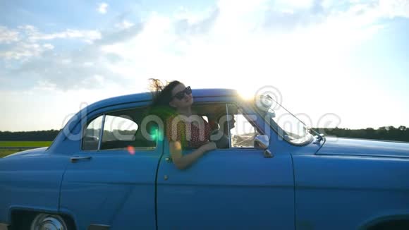 迷人的女孩戴着太阳镜斜靠在老式车窗外享受旅行年轻夫妇乘坐复古车旅行视频的预览图