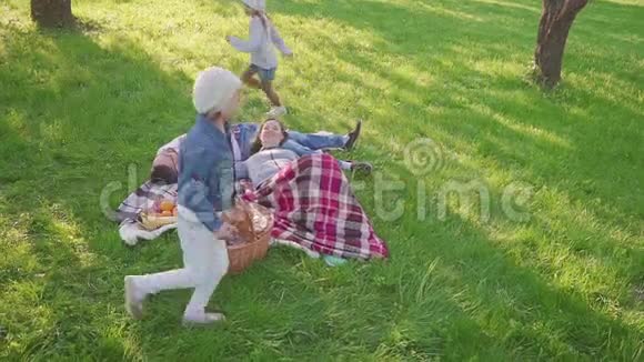 父母躺在草地上他们的两个女儿在公园里玩得很开心也有跑步的背景家庭度假景观视频的预览图