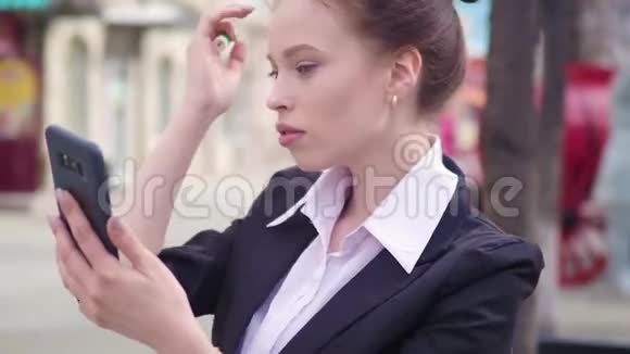 街上的商务女士用一台前置智能手机摄像头作为镜子来描绘嘴唇视频的预览图