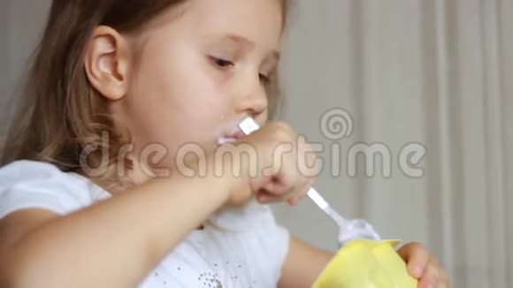 小女孩吃乳制品酸奶小孩用勺子吃奶酪肖像特写视频的预览图