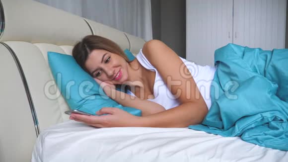 睡在床上的可爱女人使用智能手机应用程序写信息视频的预览图