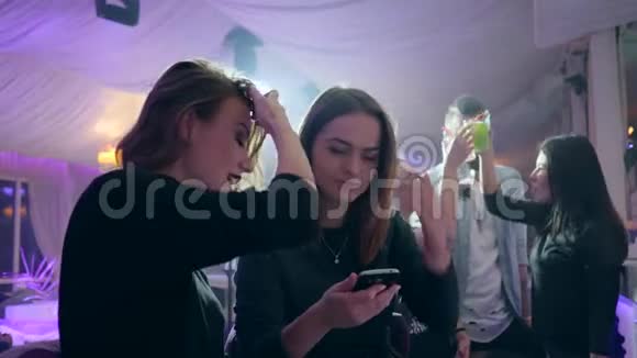 女孩们看着手机屏幕在俱乐部酒吧柜台后面的lumiere的背景下视频的预览图