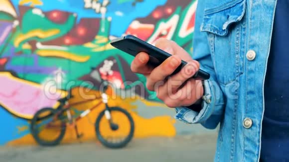 一个男人手里拿着手机站在涂鸦墙和自行车旁边视频的预览图