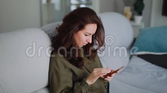 漂亮的女人坐在沙发上用智能手机视频的预览图
