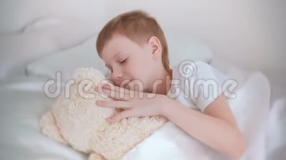 七岁的男孩醒来抚摸着躺在床上的玩具熊视频的预览图
