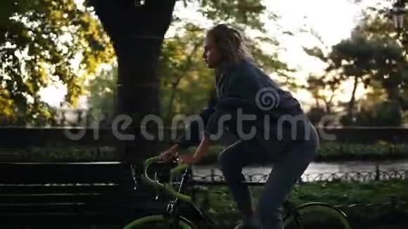 漂亮的女性在早晨公园或林荫大道骑自行车一位骑着徒步自行车的年轻女子的侧景视频的预览图