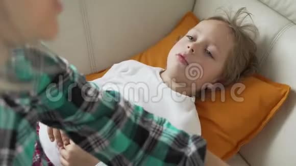 小男孩坐在沙发上头上戴着较冷的凝胶用温度计测量温度并照顾她视频的预览图