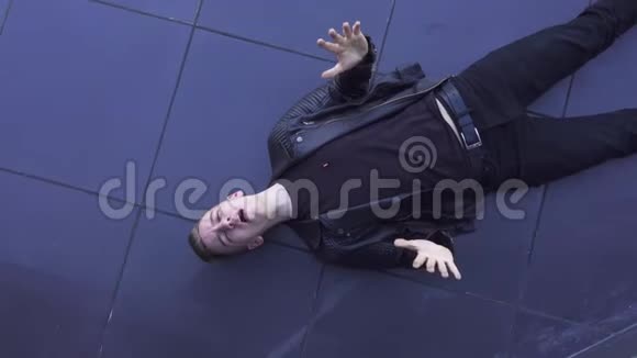可爱的年轻白种人金发男人穿着皮夹克躺在深色瓷砖地板上视频的预览图