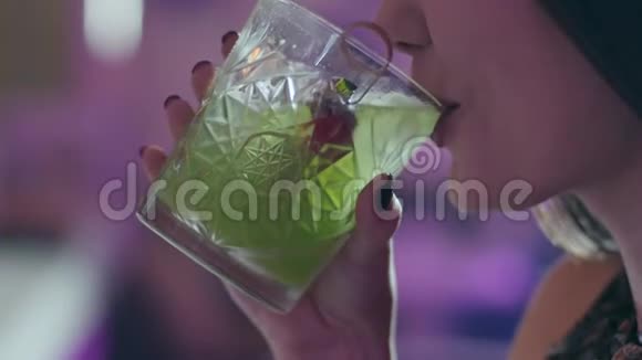 年轻女子喝绿色鸡尾酒用透明玻璃装饰草莓并在夜间特写时微笑视频的预览图