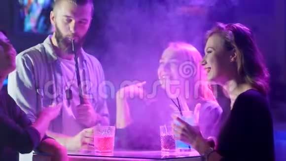 吸烟的年轻人微笑着举起酒杯中的有色饮料在俱乐部的餐桌旁举杯庆祝视频的预览图