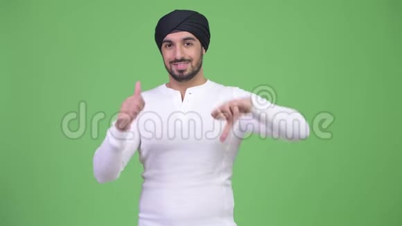年轻的满脸胡须的印度男人在竖起大拇指和竖起大拇指之间做出选择视频的预览图