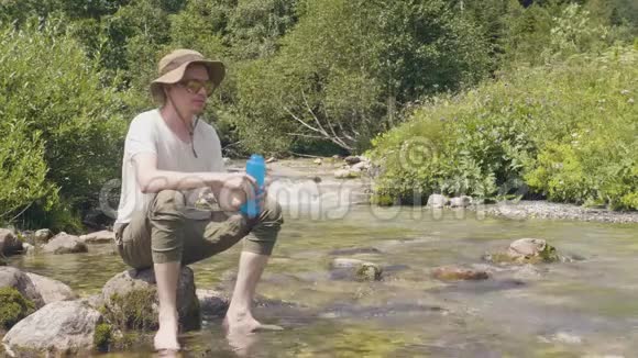 海克人在山林的河岸边喝着瓶里的泉水视频的预览图