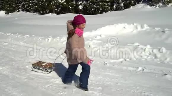 一个快乐的女孩在冬天的山上穿过一片雪林她在笑她把雪橇拉到身后慢慢视频的预览图