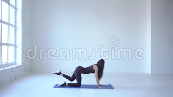 在白色工作室里瘦削的运动教练在瑜伽垫上表演运动驴踢的完整视角4k视频的预览图