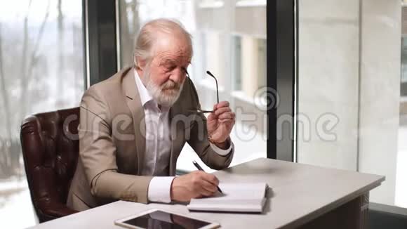 老人愉快的人正在室内的笔记本上写他的想法视频的预览图