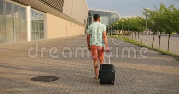 非洲男子穿着短裤t恤和耳机将手提箱拉到机场后景为假期做好准备视频的预览图