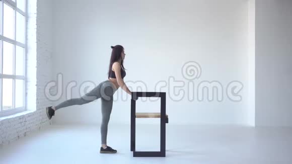 初学者的运动练习年轻的sporswoman正在做那个蹲式的回扣而她则斜靠在白色的椅子上视频的预览图