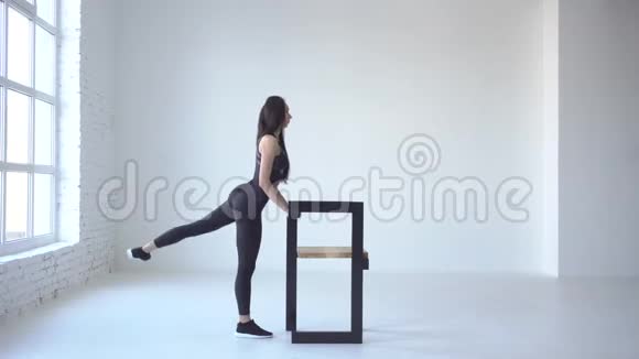 运动的黑发教练在白色独立工作室的椅子的帮助下表演蹲式回扣4k视频的预览图