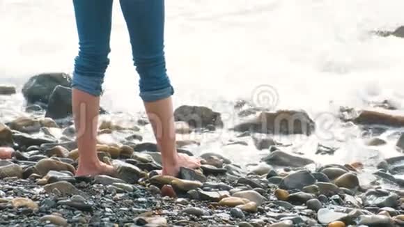 女人站在海浪中的石滩上穿着牛仔裤特写视频的预览图