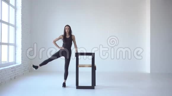 穿运动服的女运动员在白色工作室的椅子的帮助下表演侧踢4K录像视频的预览图