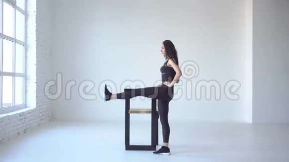 瘦骨嶙峋的女教练正在白色的独立工作室里靠在椅子上踢腿侧面全景视频的预览图