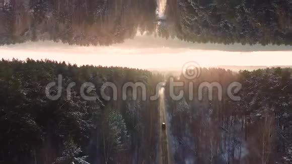 车行驶在森林中的冬季乡村道路上鸟瞰日落天空背景镜面视界效果车辆视频的预览图