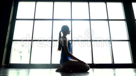 在阳光明媚的日子里女人在窗户背景下练习瑜伽白人年轻女孩做瑜伽运动运动女孩视频的预览图