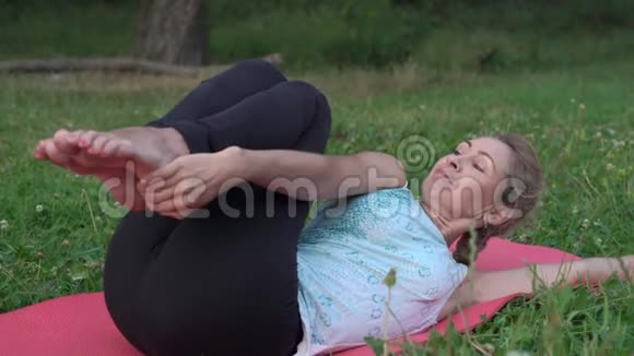 苗条的女人在城市公园的早晨在地毯上表演瑜伽体式视频的预览图