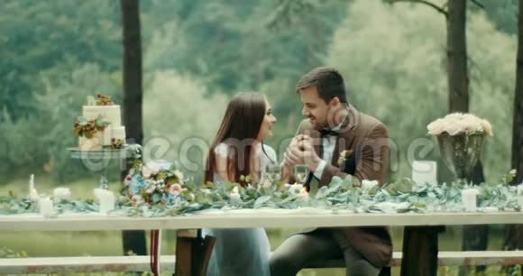 幸福的一对相爱的夫妻正在聊天轻轻地牵着手坐在桌旁用树叶鲜花和视频的预览图