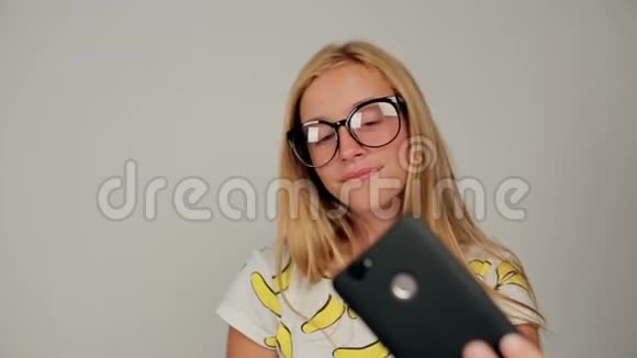 美丽的金发女郎戴着眼镜在智能手机上自拍视频的预览图